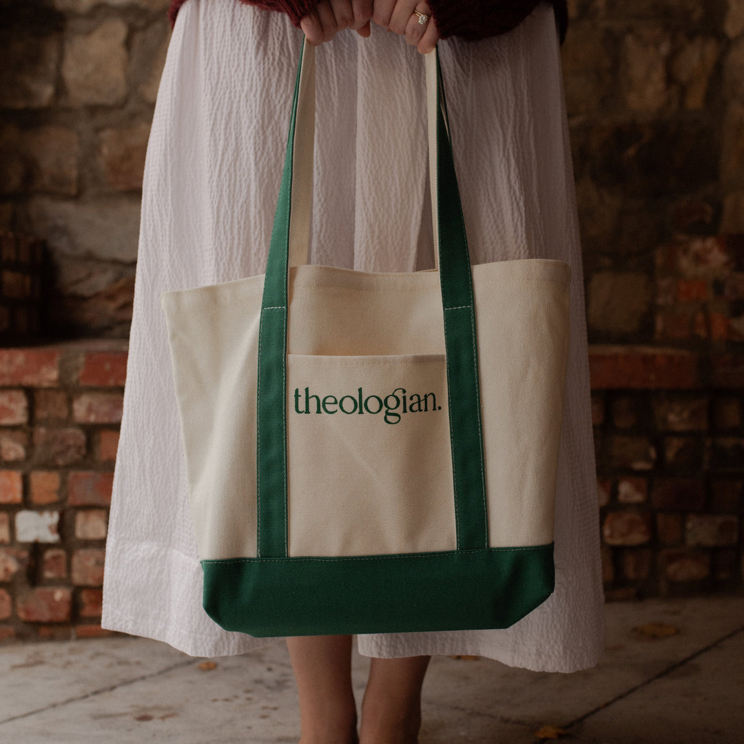 A woman with a red sweater and a white skirt holding a bag that says theologian on it  facing the camera