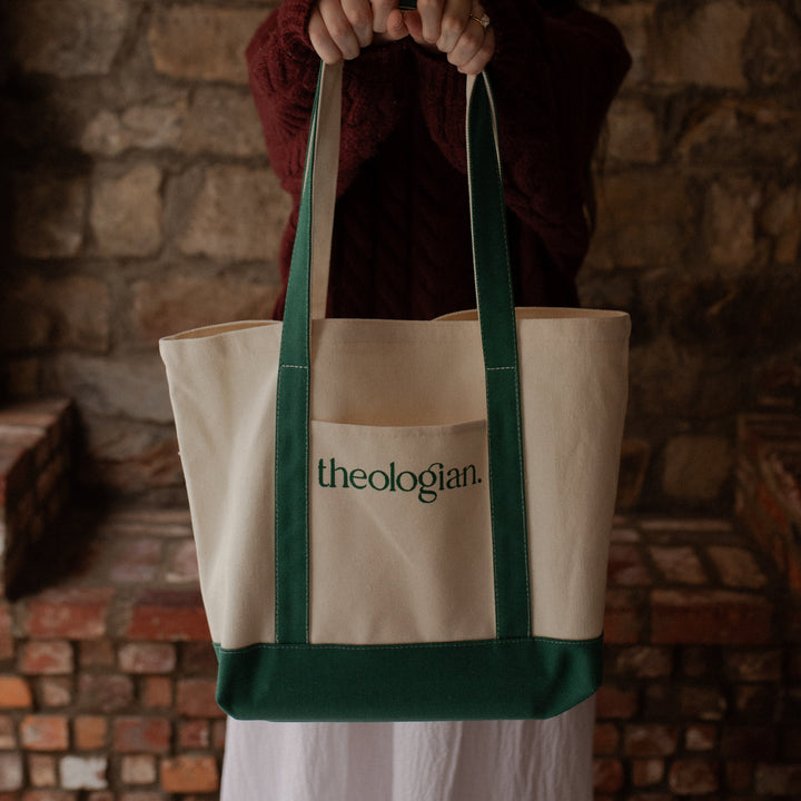 A woman with a red sweater holding a bag that says theologian on it over her shoulder toward the camera
