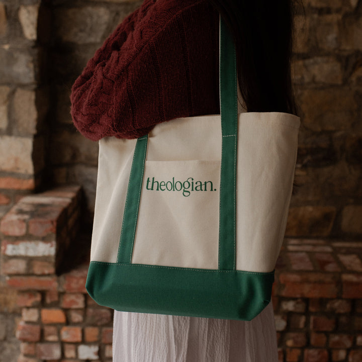 A woman with a red sweater and a white skirt holding a bag that says theologian on it over her shoulder