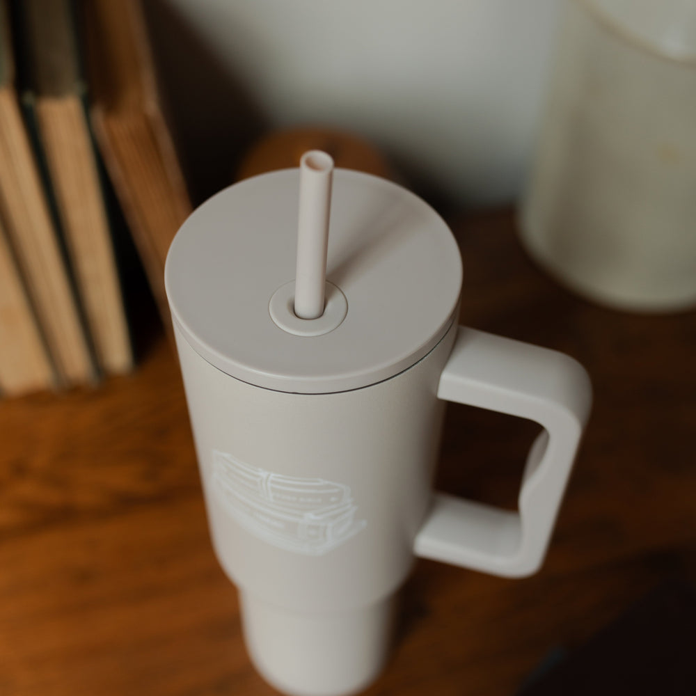 A taupe tumbler with an image of stacked books on it on a wooden desk