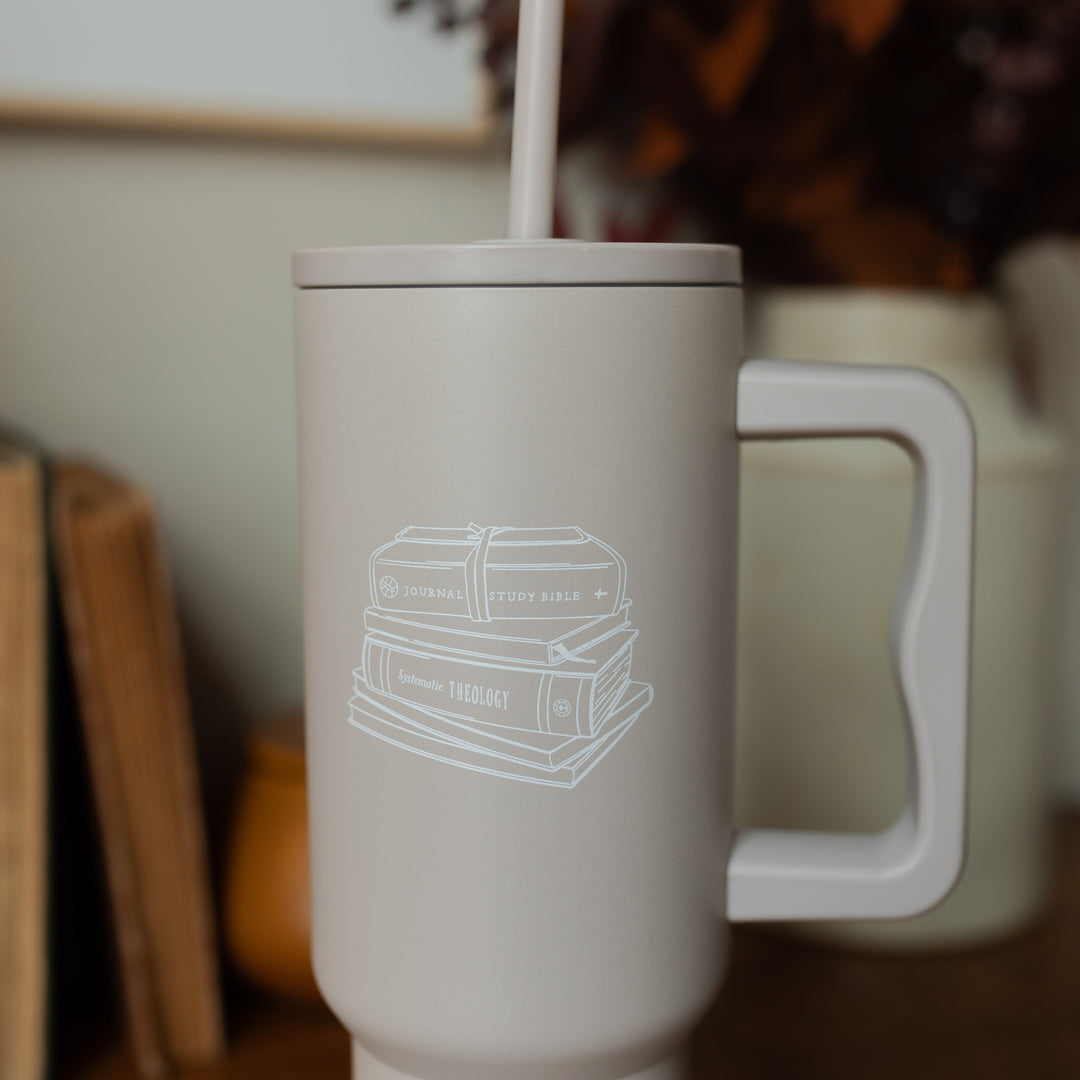 Close up of A taupe tumbler with an image of stacked books on it on a wooden desk 