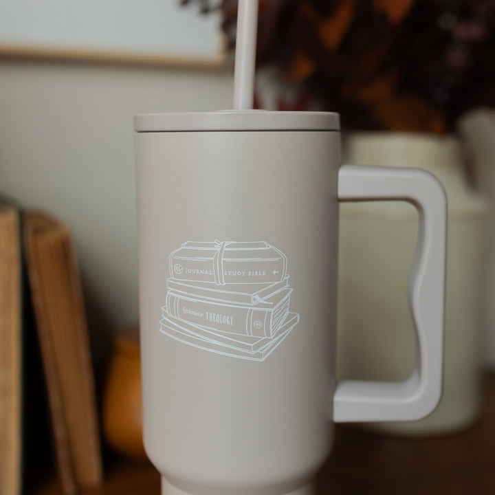 Close up of A taupe tumbler with an image of stacked books on it on a wooden desk 