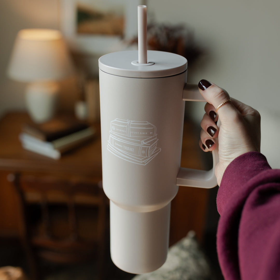 A woman holding A taupe tumbler with an image of stacked books on it