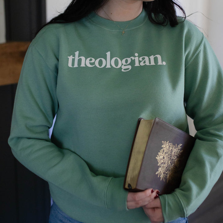 Woman wearing unisex sweatshirt that says theologian on it and holding a Bible