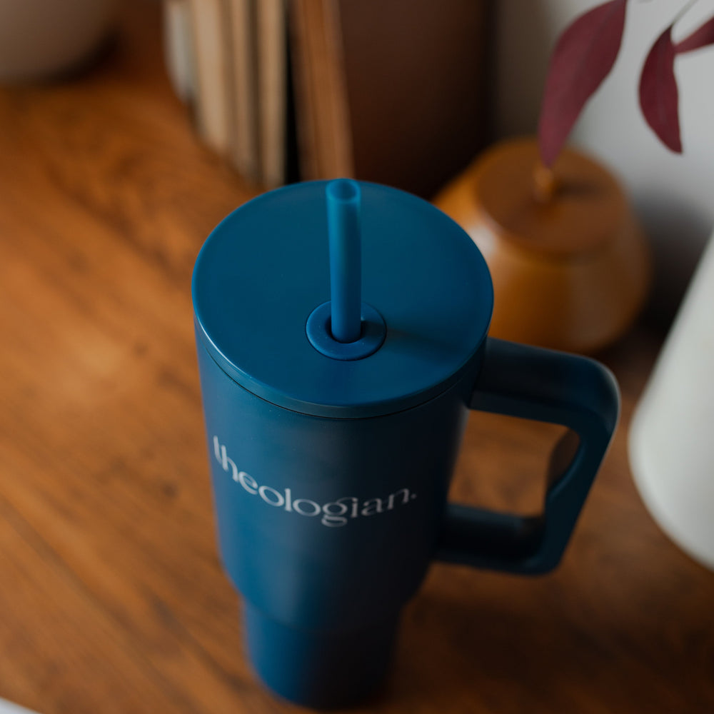 A blue tumbler with the words theologian on it on a wooden desk