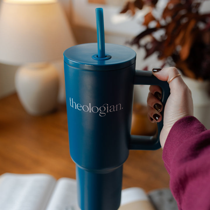 A woman holding A blue tumbler with the words theologian on it