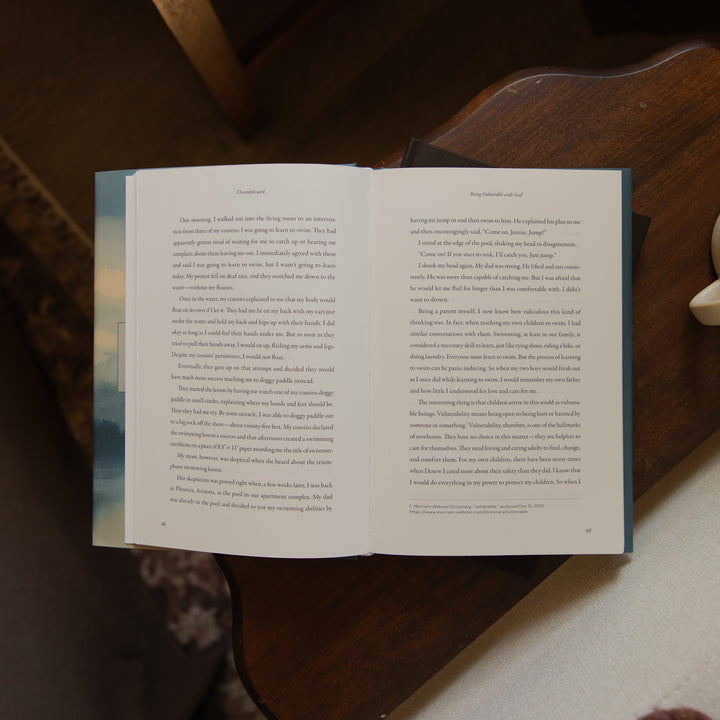 An open book showing two printed pages with black text on white paper and blue-gray covers, photographed from above on a dark wooden surface with a light fabric surface underneath.
