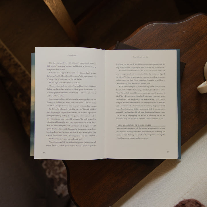 An open book with printed text spread open, photographed from above on a light surface with a dark wooden bowl in the background.