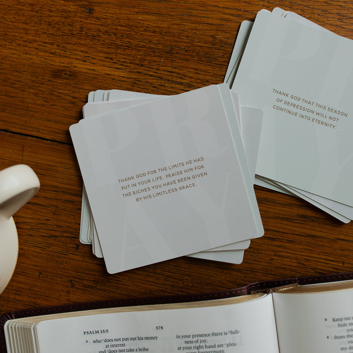 2 stacks of the Verse Cards for Depression facing the prayers on a wooden table next to a coffee cup