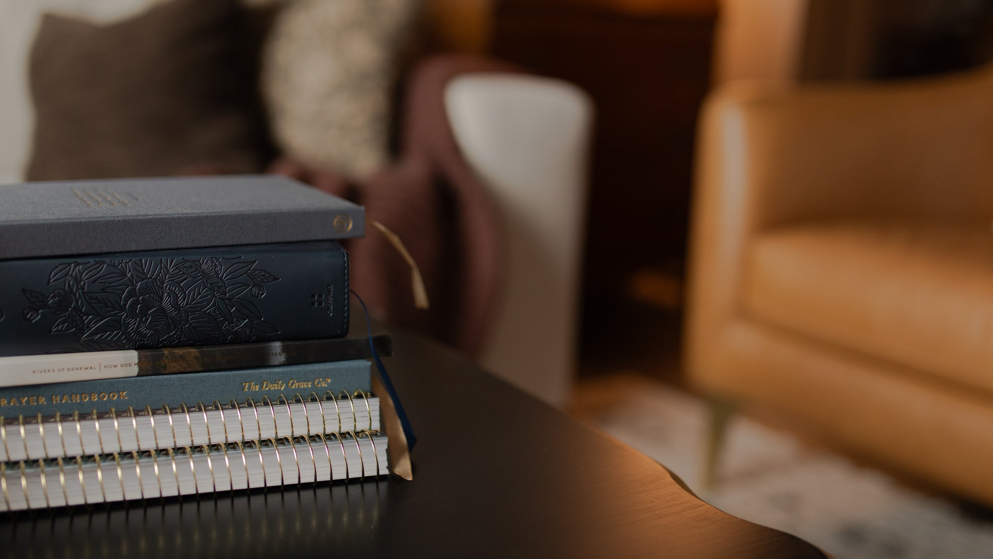 Some bible studies and a blue bible stacked on a black table with furniture in the distant background