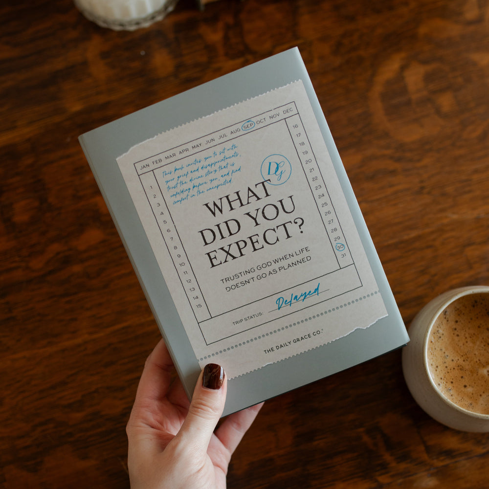 What did you expect book cover held by a woman's hand over a wooden table near a coffee cup