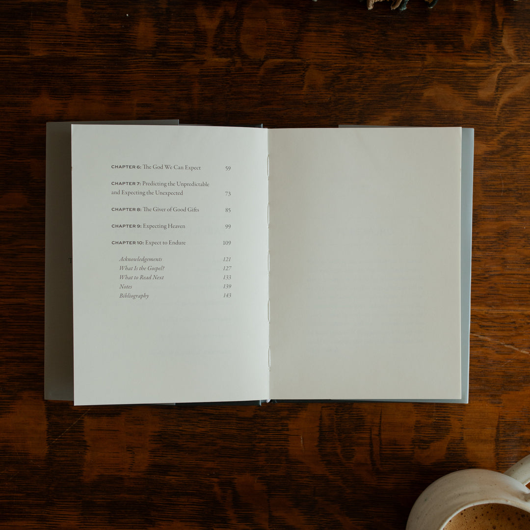 What did you expect book opened to the ending of the table of contents page on a wooden table near a coffee cup