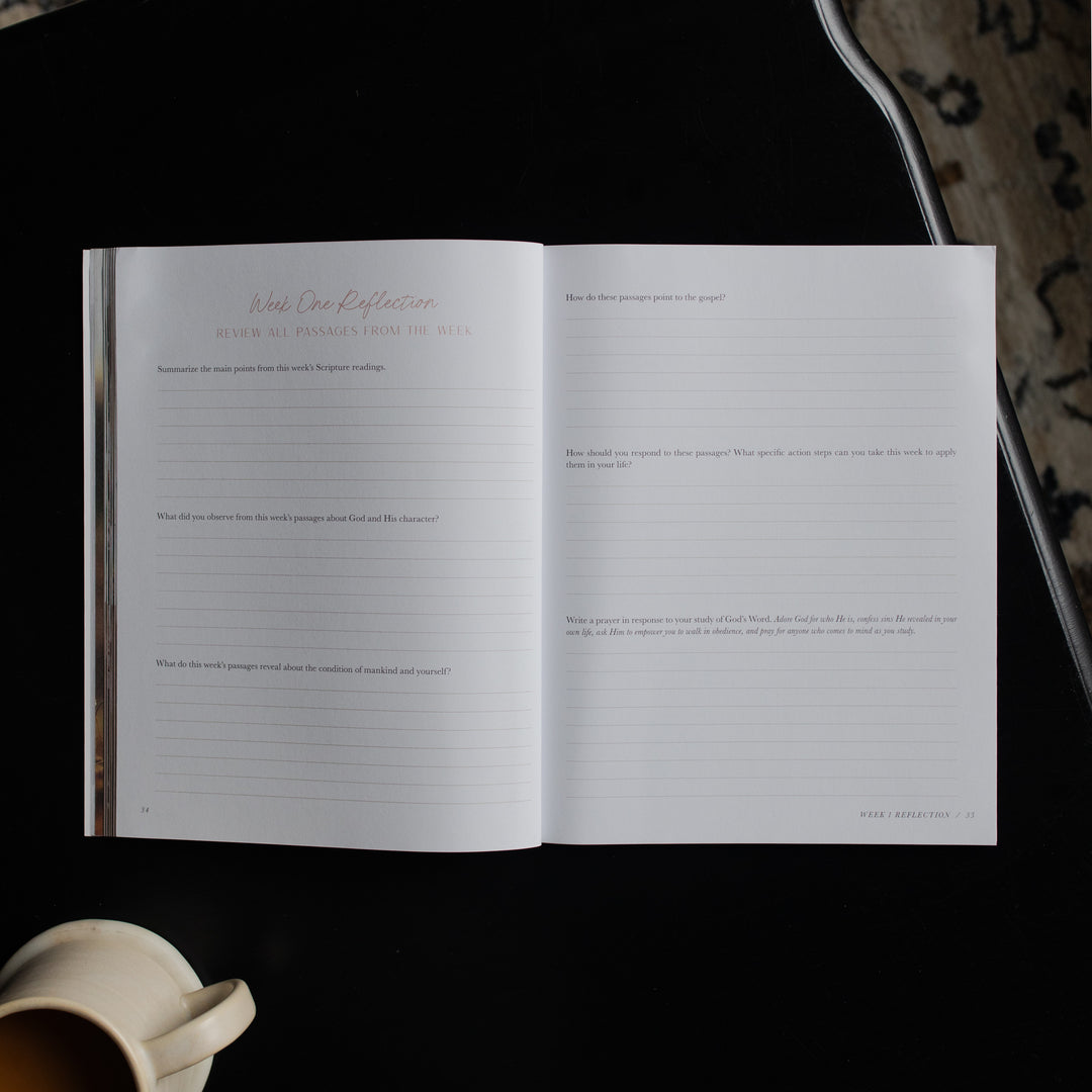 Open book with lined pages on a dark surface next to a ceramic mug.