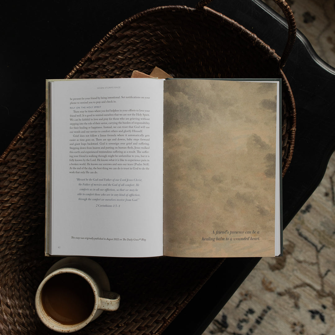 When Storms Rage opened to the Devotional Page on other books near a coffee cup in a woven basket