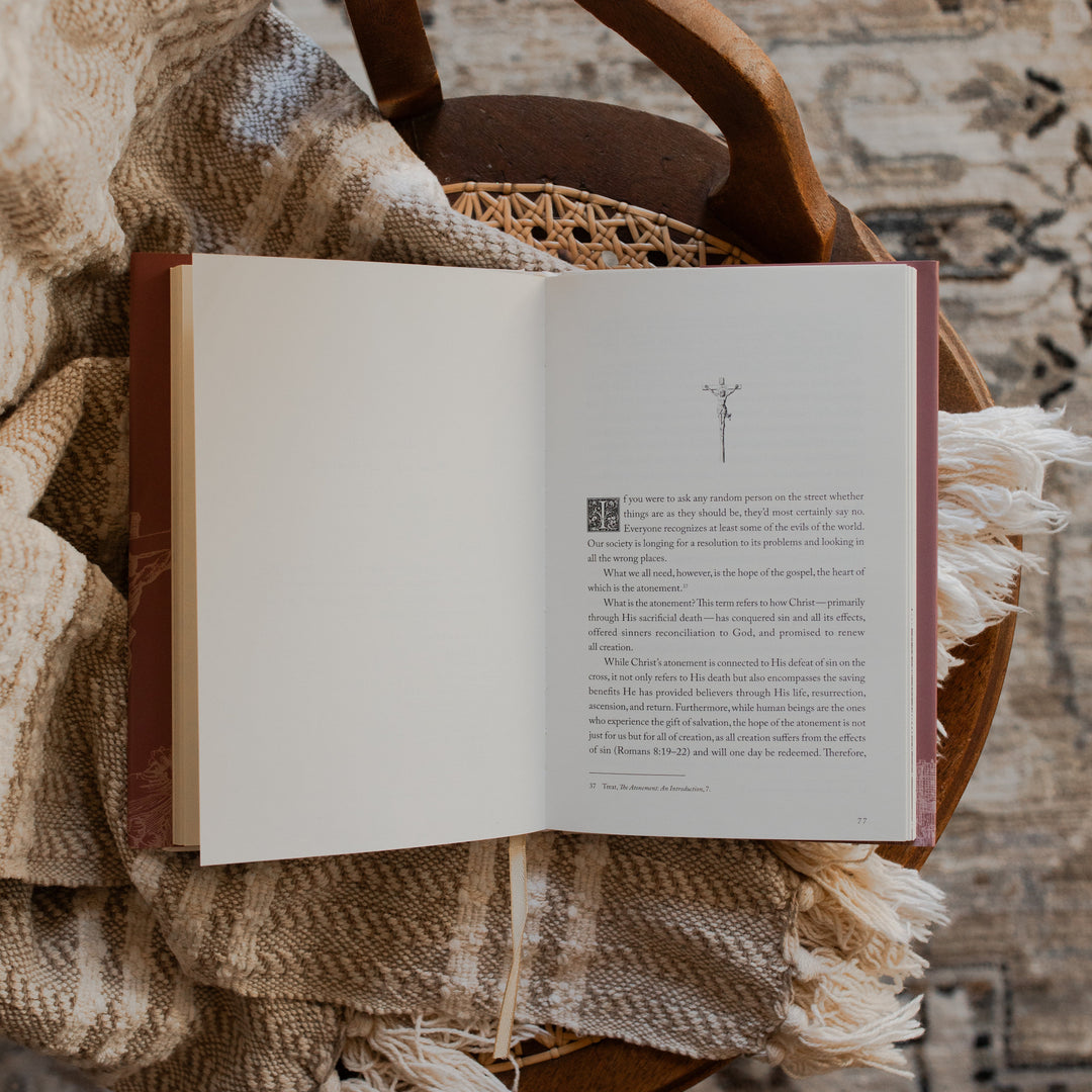 Why Did Jesus Have To Die opened to the Atonement Introduction page on a blanket and a woven chair