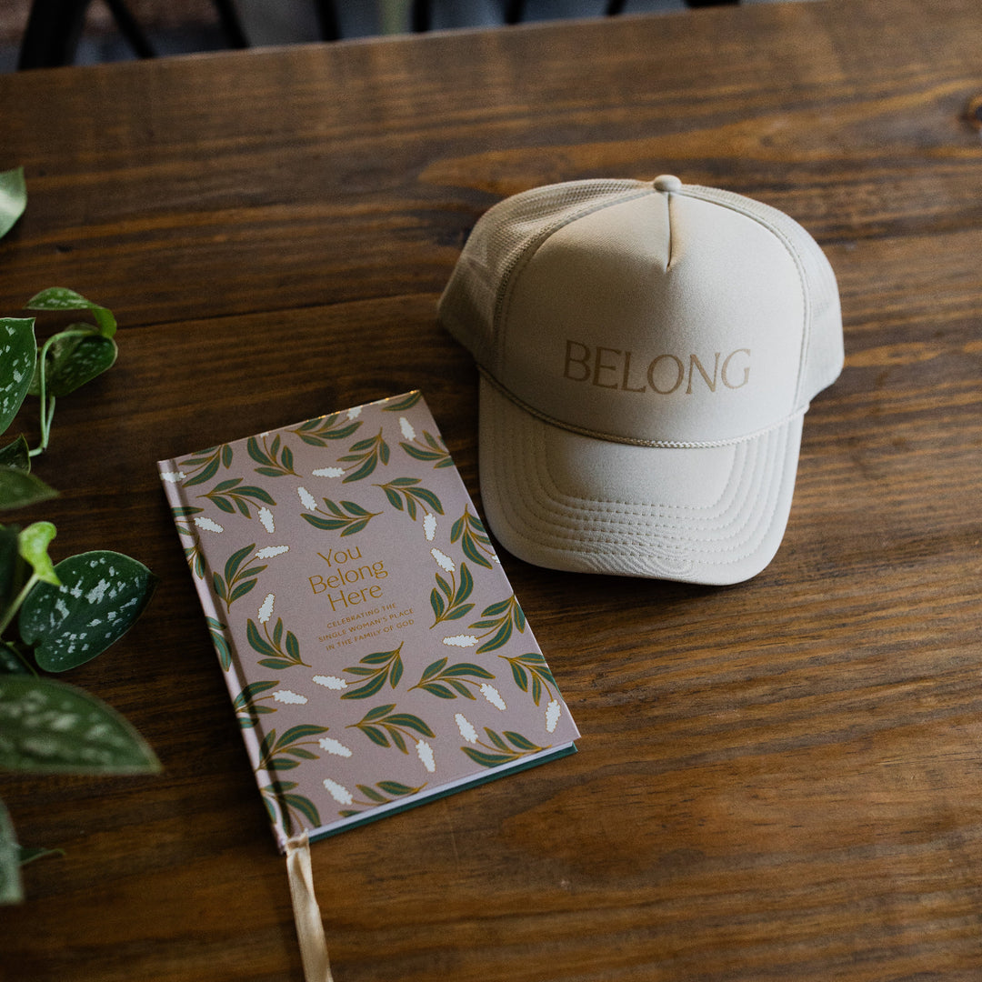 You Belong Here Study and the You Belong Here trucker hat on a wooden table next to some greenery