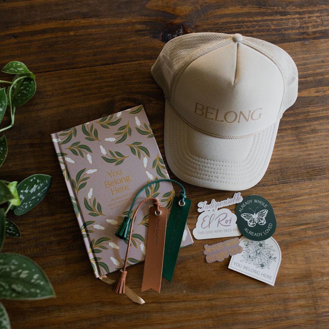 You Belong Here bookmarks on the You Belong Here Study next to the You belong here trucker hat and stickers on a wooden table next to some greenery