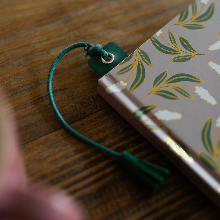 One Green You Belong Here Leatherette Bookmark inside a book on a wooden table