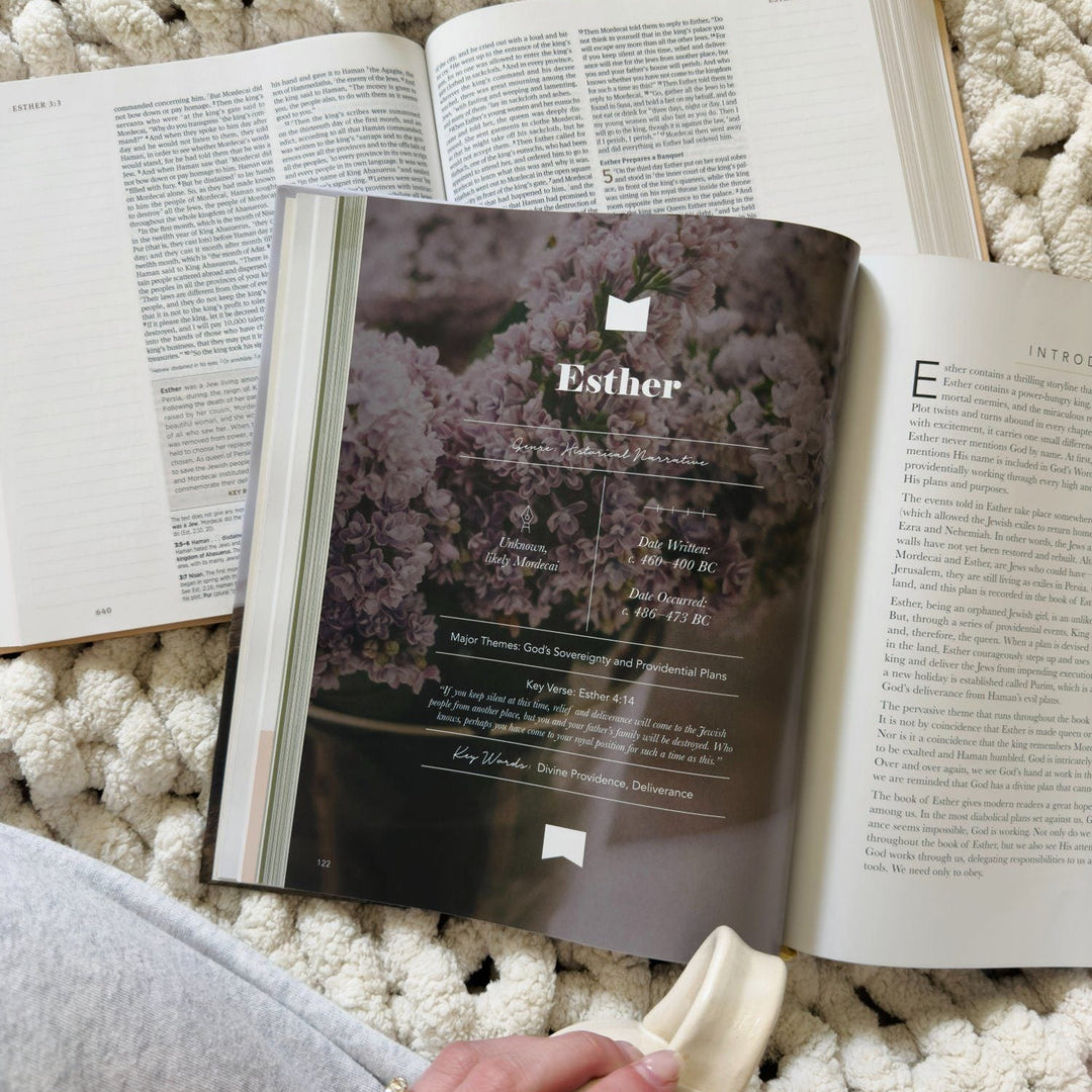 An open book with a printed page titled 'Esther' lies on a chunky cream knit blanket, with a hand holding a small cream mug in the foreground.