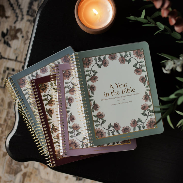 A 4 Volume set of A Year in the Bible stacked near a lit candle on a wooden black table