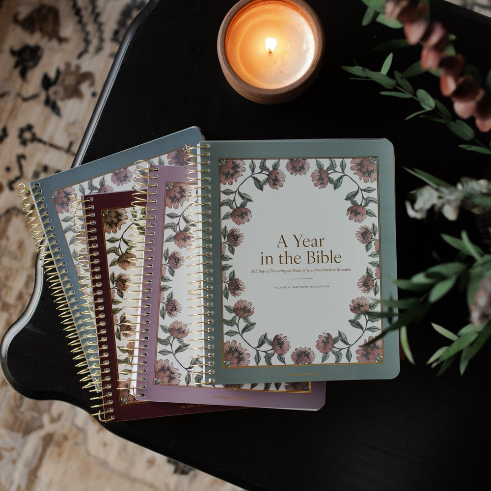 A 4 Volume set of A Year in the Bible next to a lit candle n a black wooden table