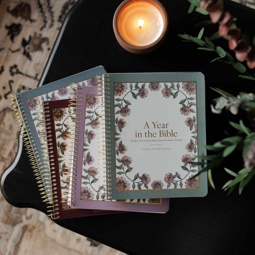 A 4 Volume set of A Year in the Bible next to a lit candle n a black wooden table