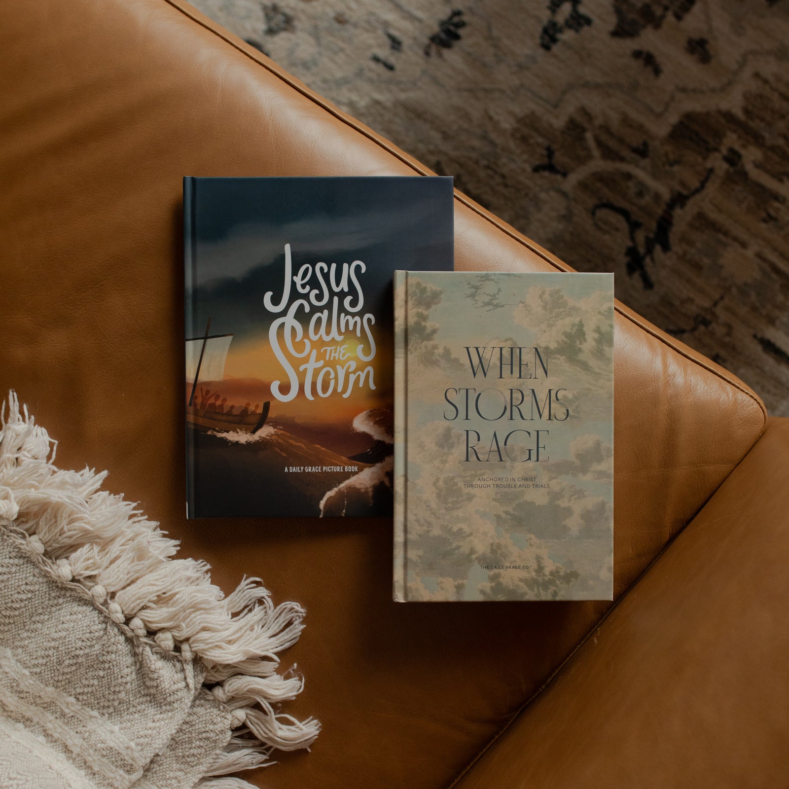 Two books titled 'Jesus Calms the Storm' and 'When Storms Rage' on a brown leather couch.