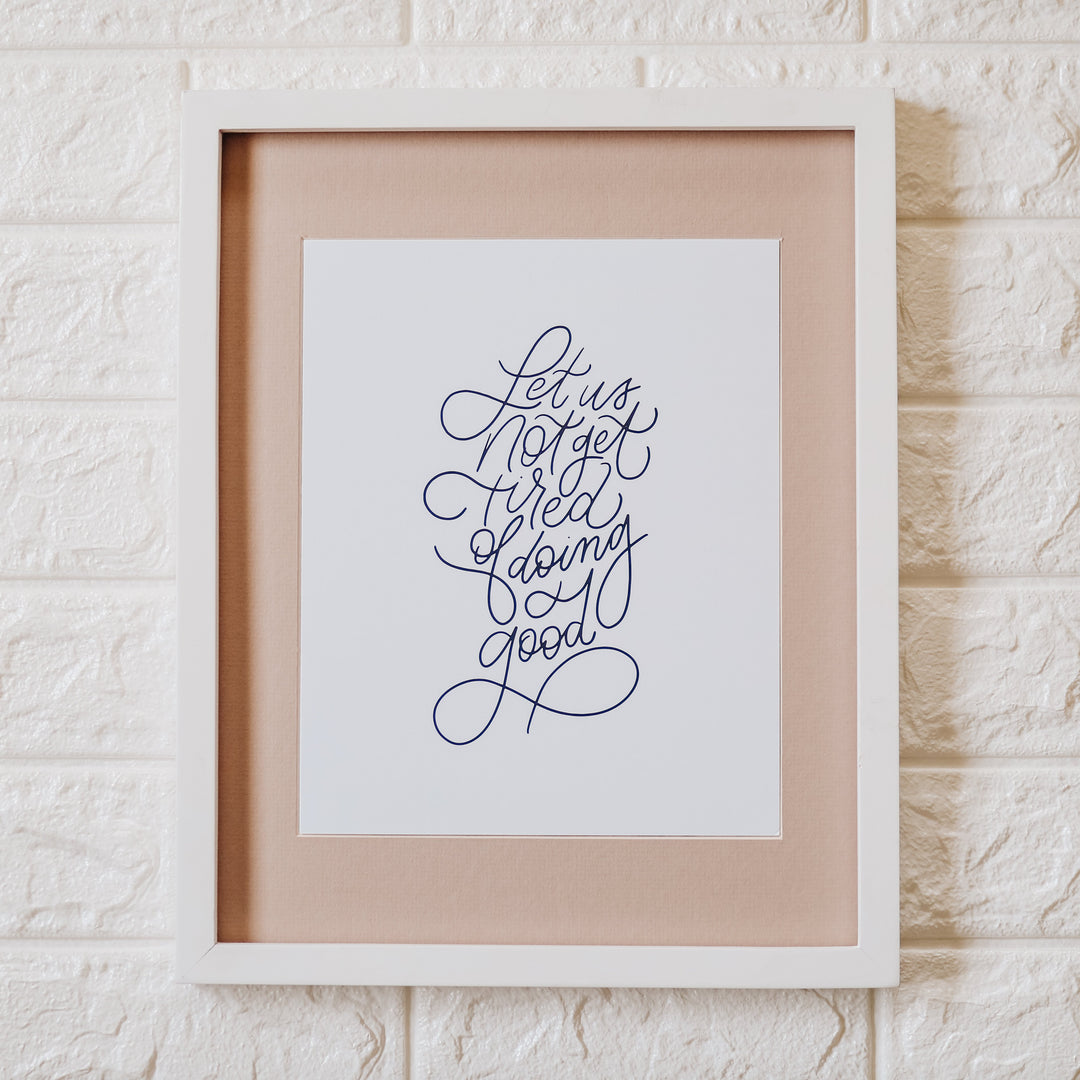 Let us not get tired print in a white frame on a white brick wall
