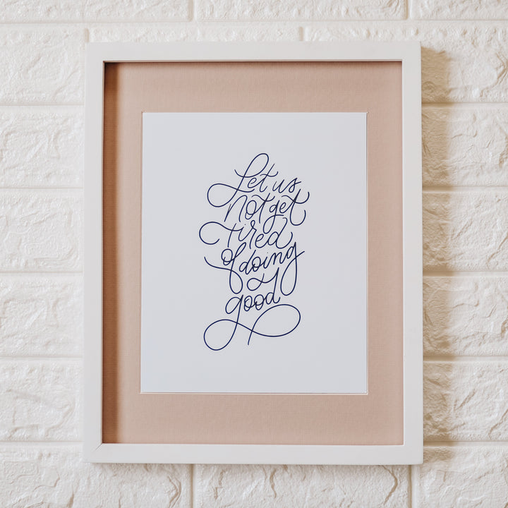 Let us not get tired print in a white frame on a white brick wall