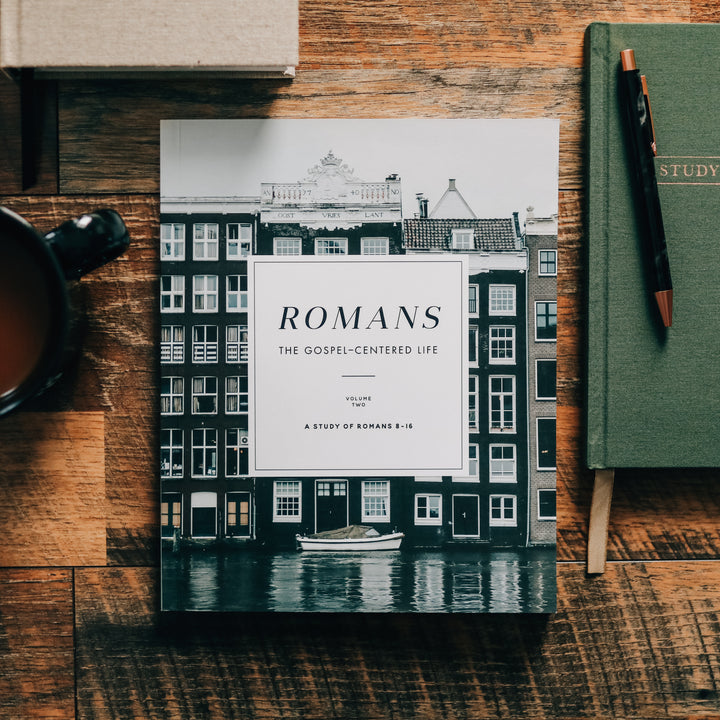 Romans Bible study on a wooden table next to a green journal.