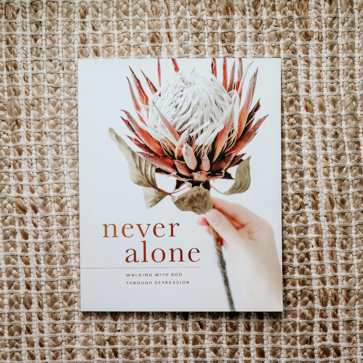 Image of the cover of the Never Alone Bible study. The cover is of a person holding a bloomed artichoke. The colors are white, red, and green. 