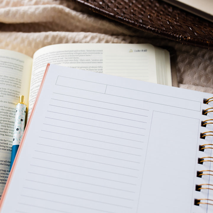 Image of an open journal on top of a Bible with a floral pen. 