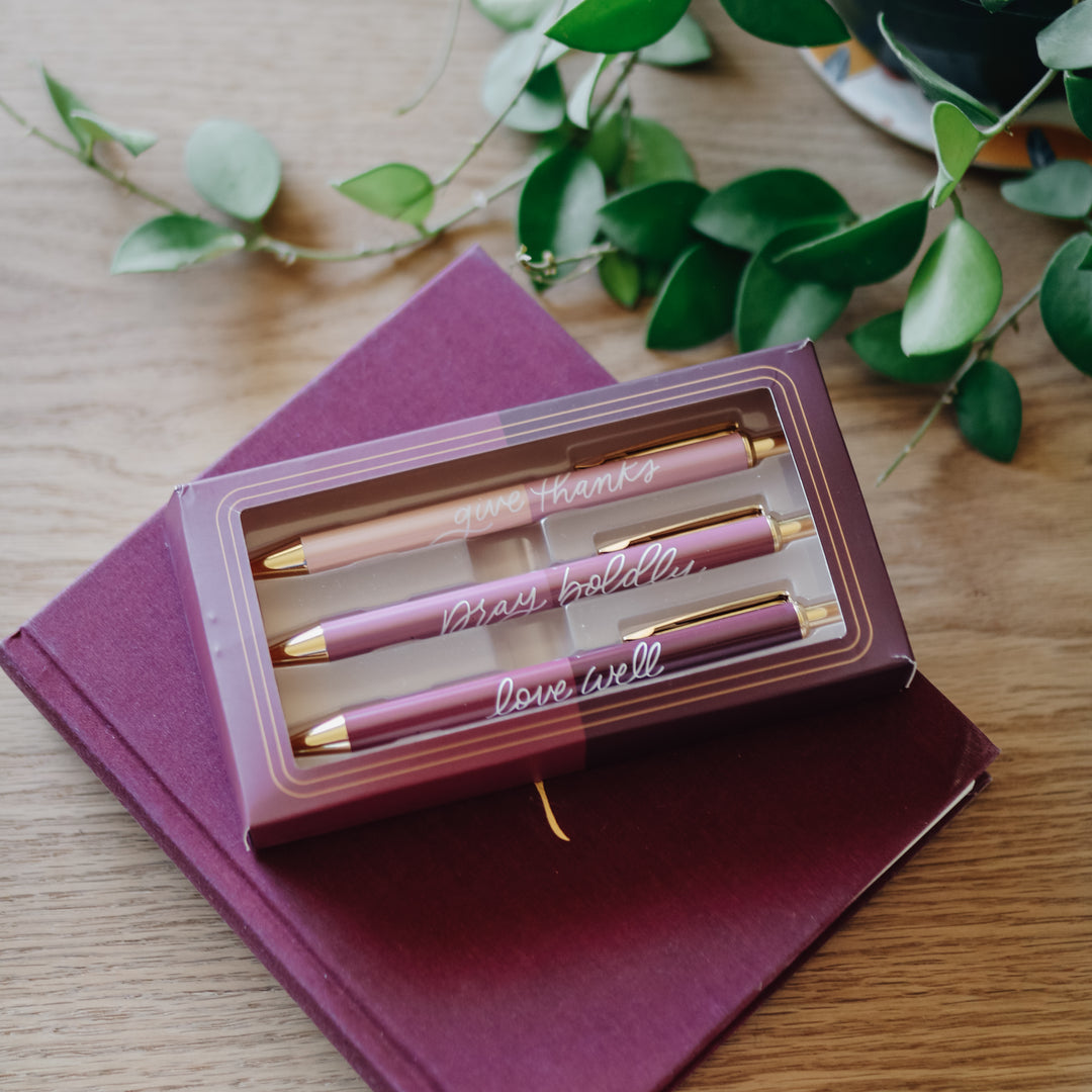 Three pink pens in a box on top of a burgundy book.