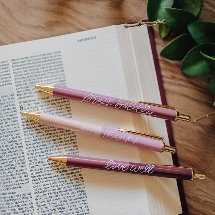 Set of three pink pens with white script on top of a Bible.