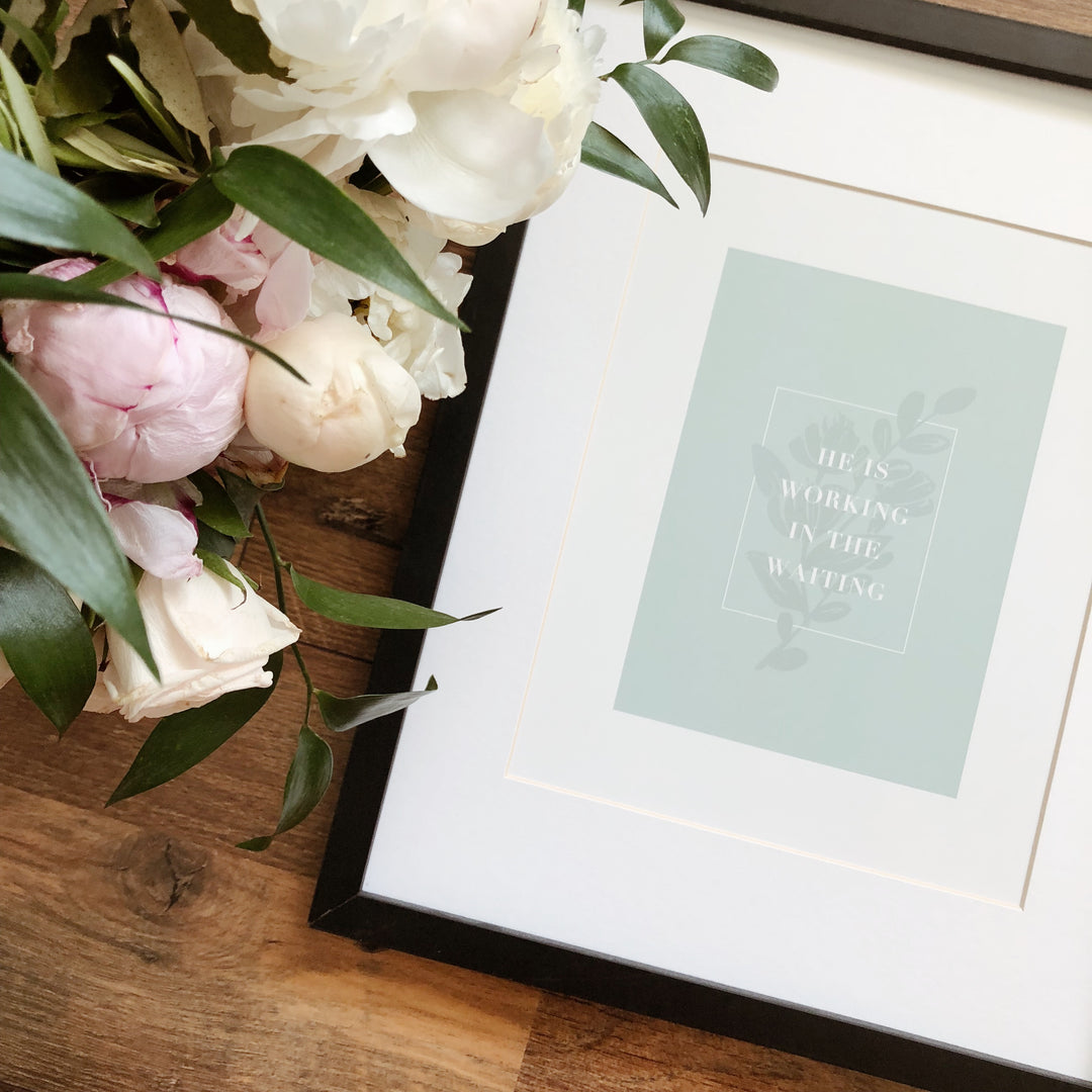 Working in the Print laying on a brown wooden table next to pink and white flowers